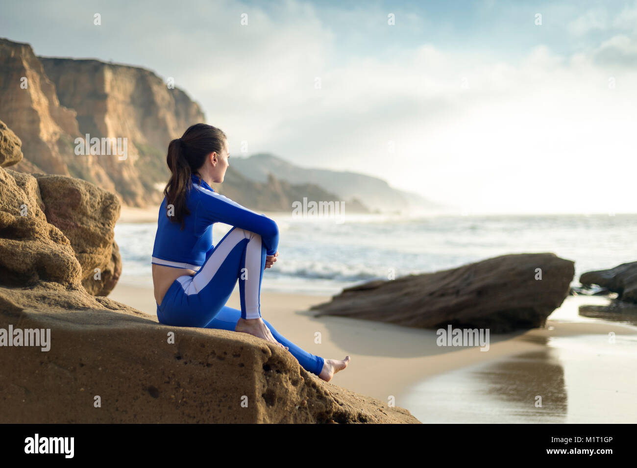 Frau trägt einen blauen Anzug im Sommer sitzen die auf Felsen beobachten die Wellen. Stockfoto