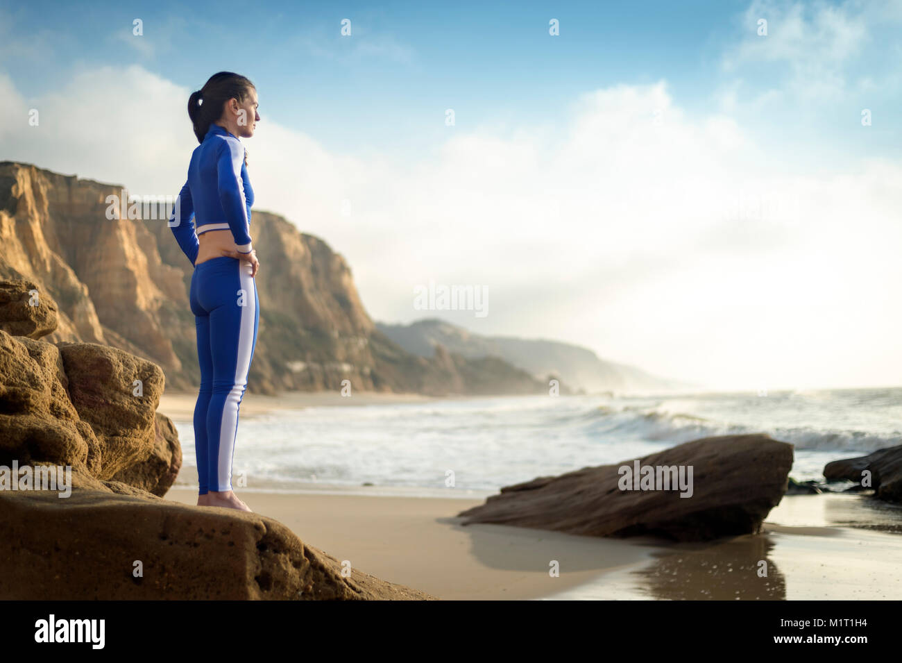 Frau trägt ein blaues Sommer Neoprenanzug stehen auf Felsen beobachten die Wellen. Stockfoto
