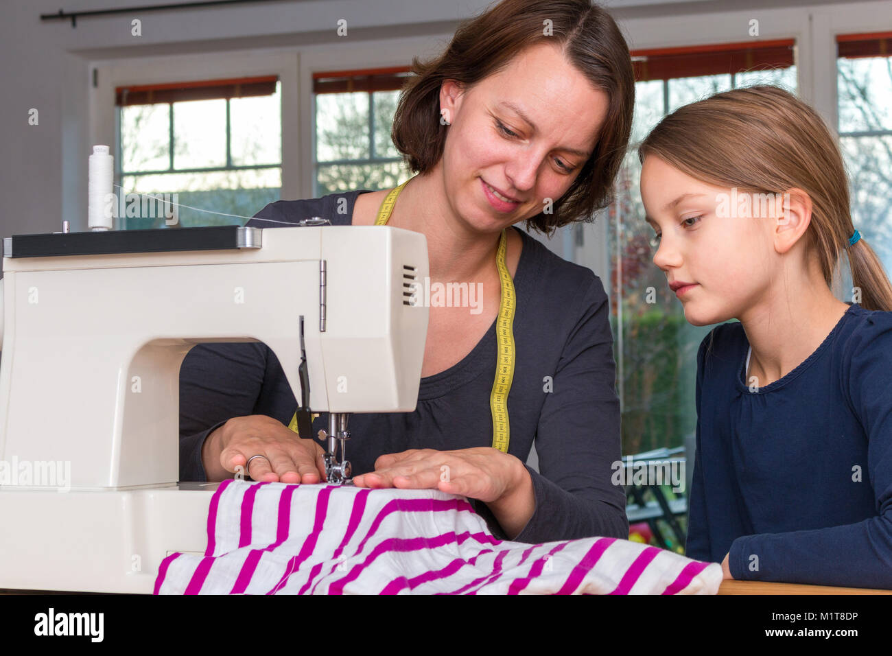 Mutter lehrt ihre 8 Jahre alte Tochter wie eine gestreifte Textilien mit einer Nähmaschine zu nähen. Stockfoto