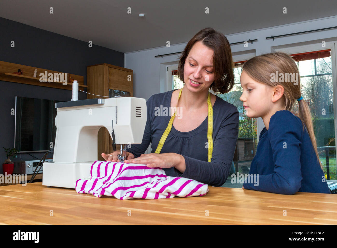 Mutter lehrt ihre 8 Jahre alte Tochter wie eine gestreifte fabics mit einer Nähmaschine zu nähen. Stockfoto