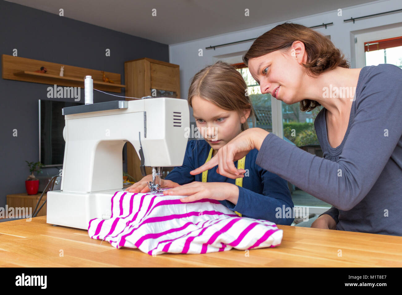 Mutter lehrt ihre 8 Jahre alte Tochter wie eine gestreifte fabics mit einer Nähmaschine zu nähen. Stockfoto