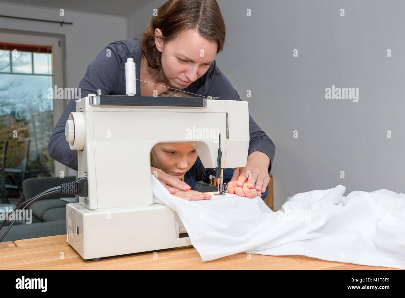 Mutter lehrt ihre 8 Jahre alte Tochter wie eine weiße fabics mit einer Nähmaschine zu nähen. Stockfoto