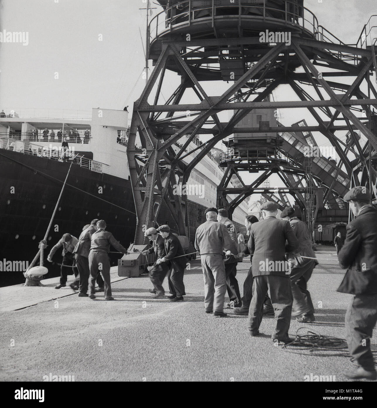 1950, historische, männliche Dockers ziehen ein Seil der RMS Queen Elizabeth Ocean Liner in an den Southampton Docks, England, UK zu binden. Nachdem die britische Königin Mutter genannt, war es das größte Passagierschiff, das jemals gebaut wurde damals (1938) und blieb für 56 Jahre danach. Sie wurde als Truppentransporter im Zweiten Weltkrieg benutzt und wurde erst ein ozeanriese wie in 1946 vorgesehen. Stockfoto
