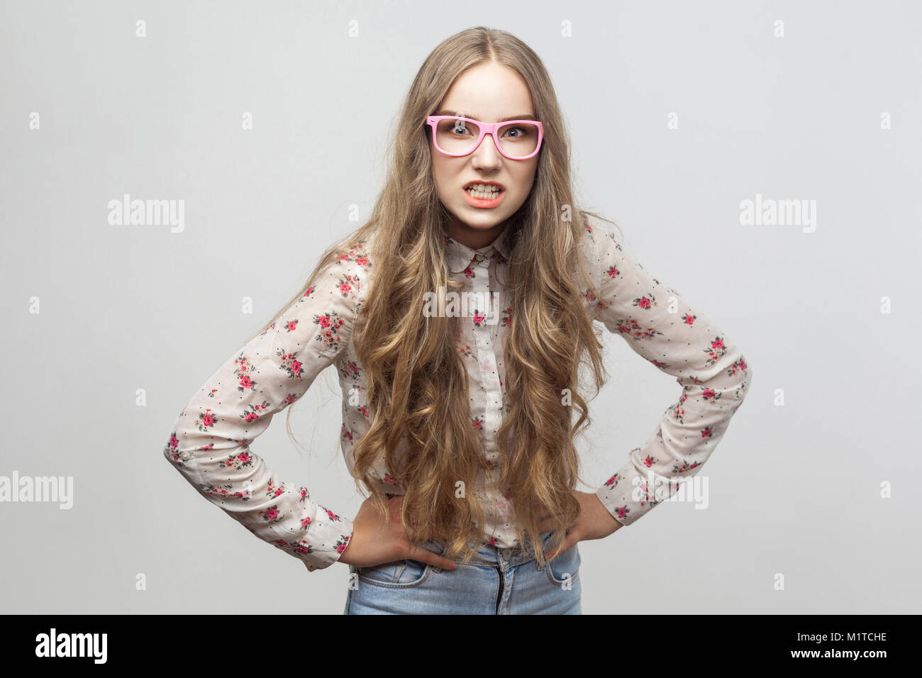 Wütende junge erwachsene Frau in rosa Brille, Hemd, an der Kamera und Brüllen. Studio gedreht. Auf grauem Hintergrund Stockfoto