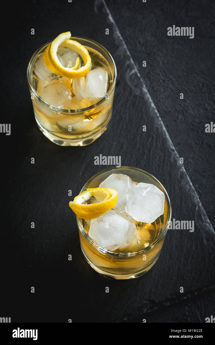 Whiskey on the rocks mit Zitronenschale. Whisky mit Eis, garniert mit Citrus Twist auf schwarzem Stein serviert, Ansicht von oben, kopieren. Stockfoto