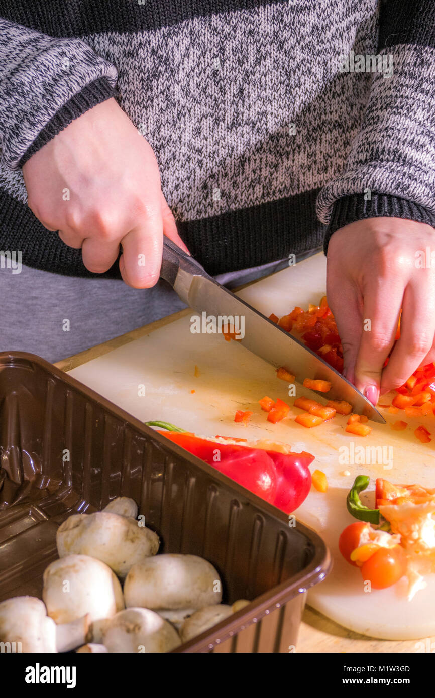 Eine Frau (nur Hände) hacken ein roter Pfeffer mit einem großen, scharfen, Edelstahl Messer. Auf einem Schneidebrett aus Kunststoff. UK. Stockfoto