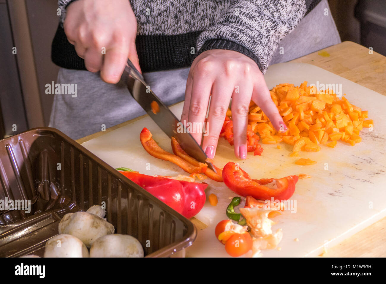 Eine Frau (nur Hände) hacken ein roter Pfeffer auf einem Brett mit einem großen, scharfen, Edelstahl Messer, mit anderen Gemüse in der Nähe. UK. Stockfoto