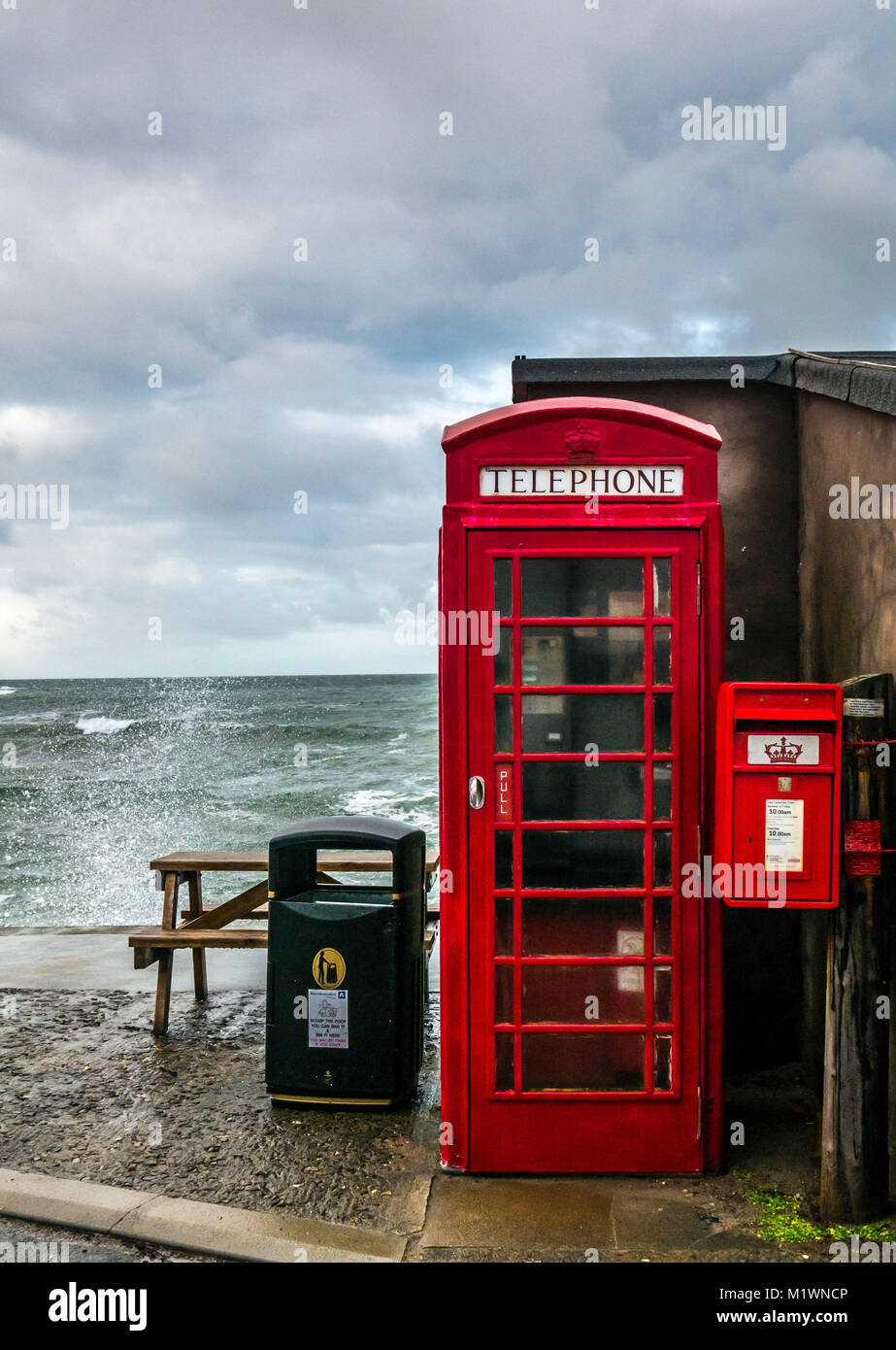 Pennan, Aberdeenshire, Schottland, Vereinigtes Königreich. Die starken Winde erzeugen eine Welle in der Nordsee entlang der Nordostküste Schottlands, mit großen Wellen, die gegen die Promenade in dem malerischen Dorf plätschern, das berühmt ist für seinen Film Local Hero. Die ikonische britische rote Telefonbox, ursprünglich eine Filmrequisite, wurde später als Folge der öffentlichen Nachfrage installiert Stockfoto
