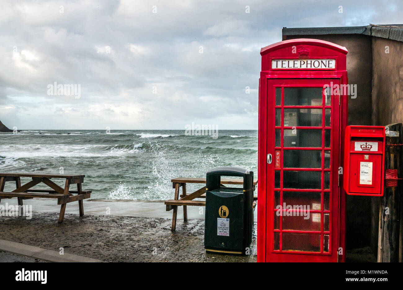 Pennan, Aberdeenshire, Schottland, Vereinigtes Königreich. Die starken Winde erzeugen eine Welle in der Nordsee entlang der Nordostküste Schottlands, mit großen Wellen, die gegen die Promenade in dem malerischen Dorf plätschern, das berühmt ist für seinen Film Local Hero. Die ikonische britische rote Telefonbox, ursprünglich eine Filmrequisite, wurde später als Folge der öffentlichen Nachfrage installiert Stockfoto