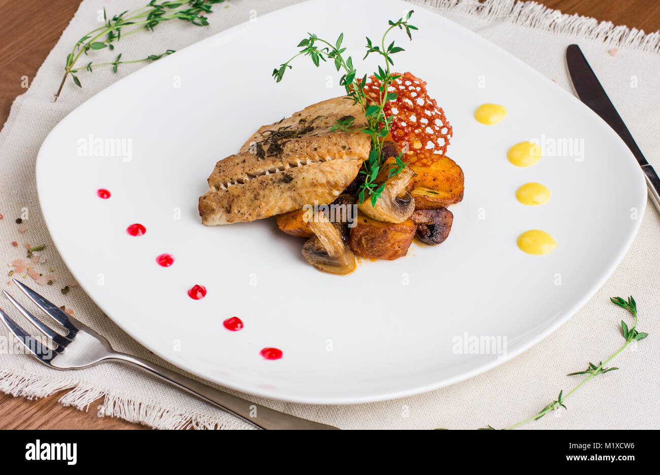 Gebackener Fisch mit Kartoffeln und Pilze auf eine weisse Platte Stockfoto