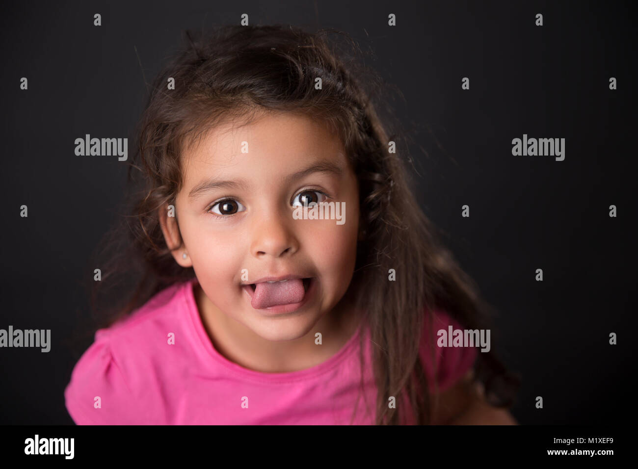 Cute Baby Girl, die Zunge an der Kamera vor der schwarzen Hintergrund. Stockfoto