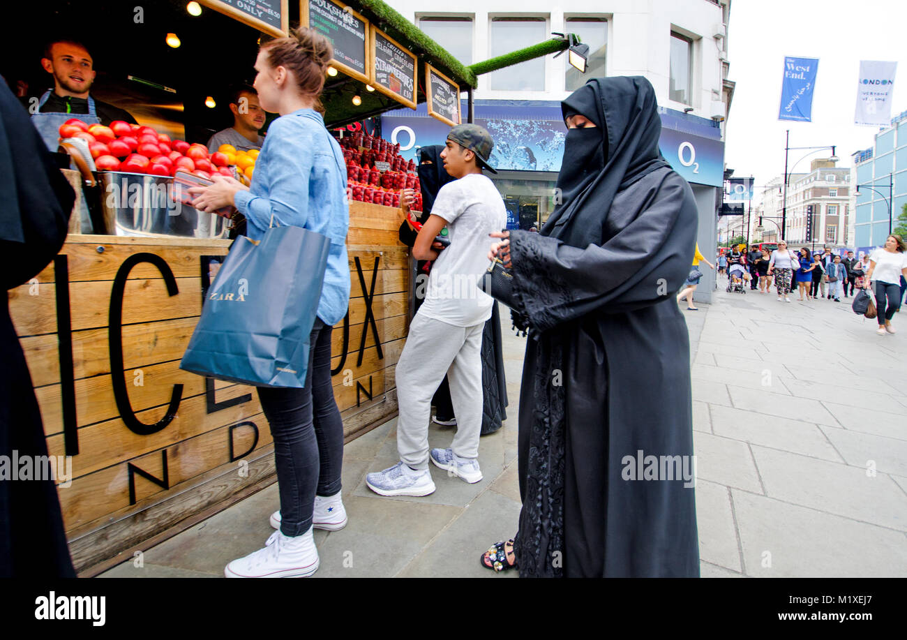 London, England, UK. Muslimische Frau in voller Länge islamische Kleidung in einem Stall verkaufen Obst Stockfoto