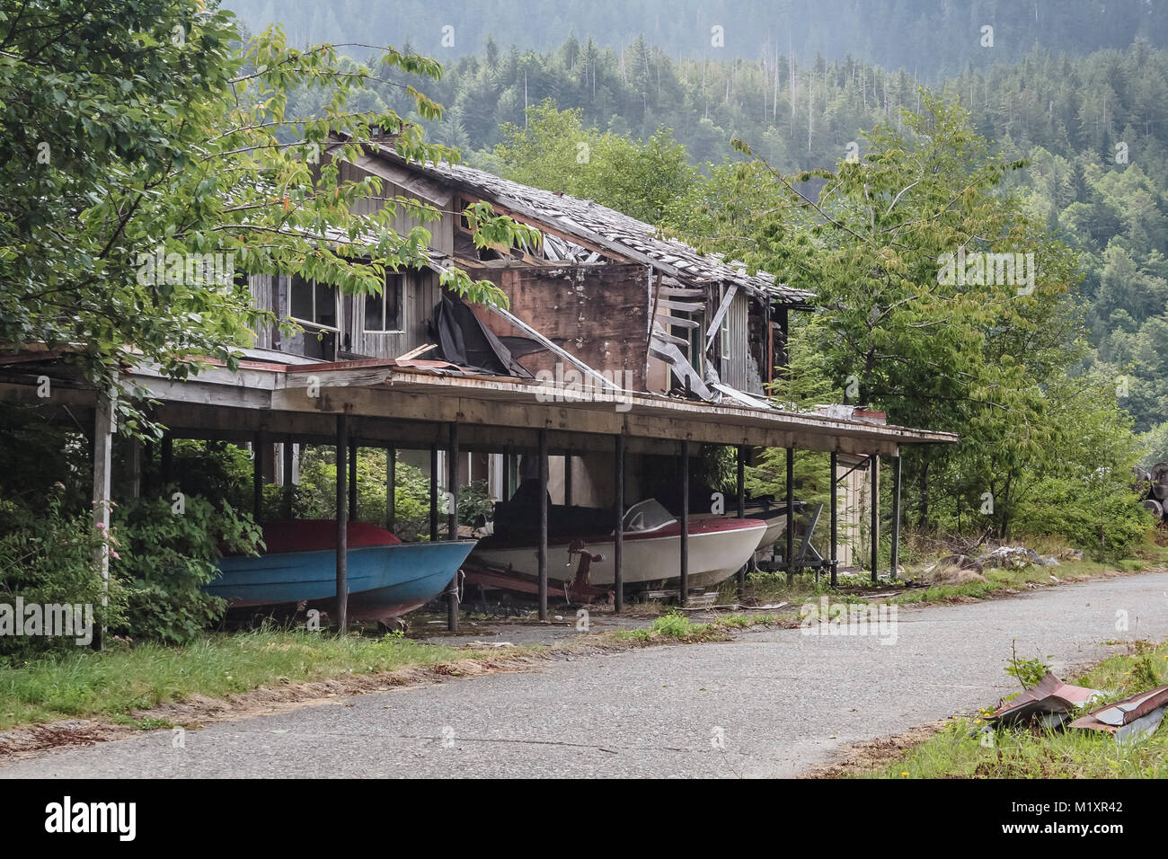 Mit Obstbäumen daneben und Boote und Trailer noch in den Carport, ein verlassenes Haus steht in Ruinen in der Geisterstadt Ozean fällt, BC. Stockfoto
