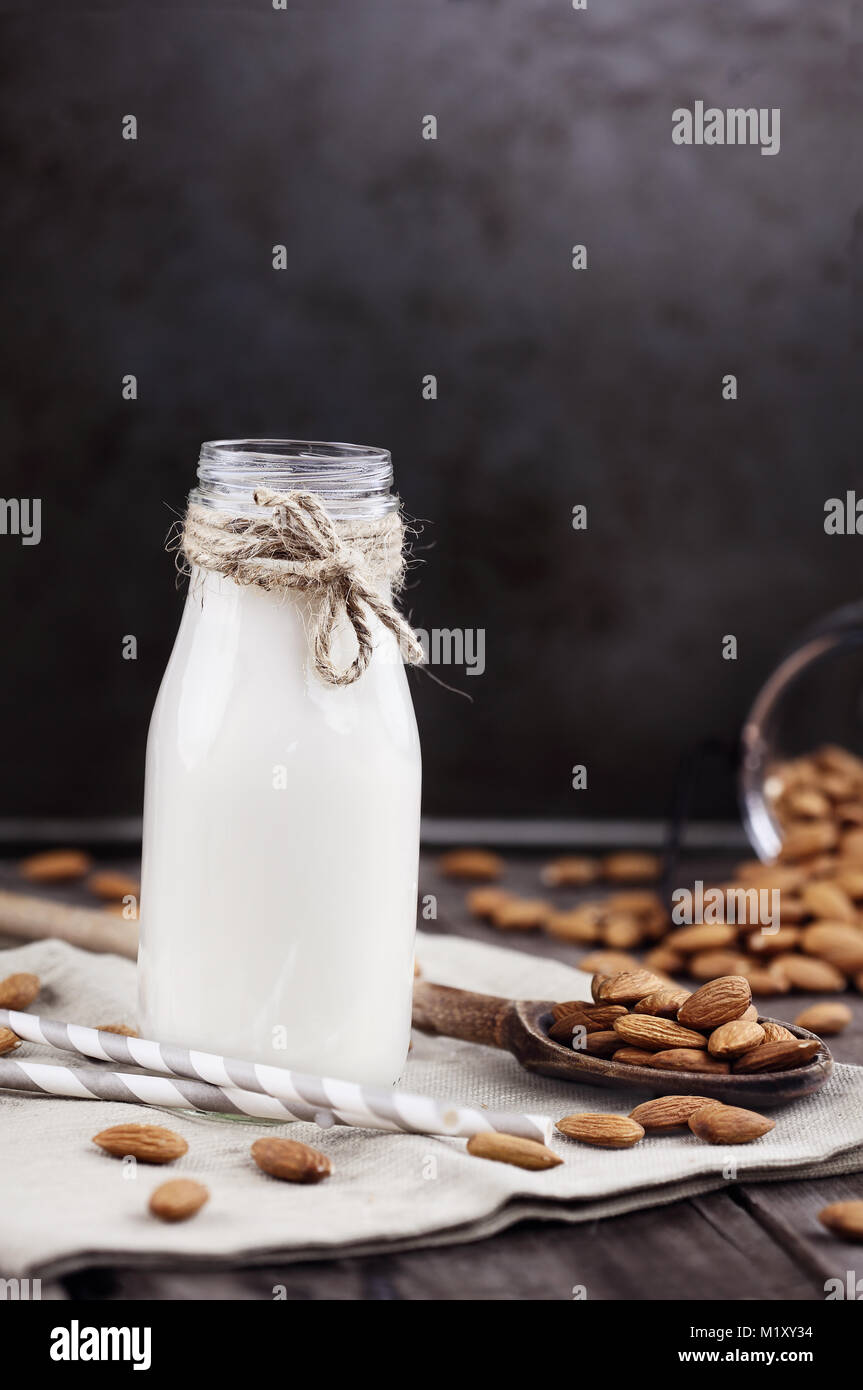 Organische weiße Mandelmilch in einer Glasflasche mit ganzen Mandeln über einen rustikalen Holztisch verschüttet. Stockfoto