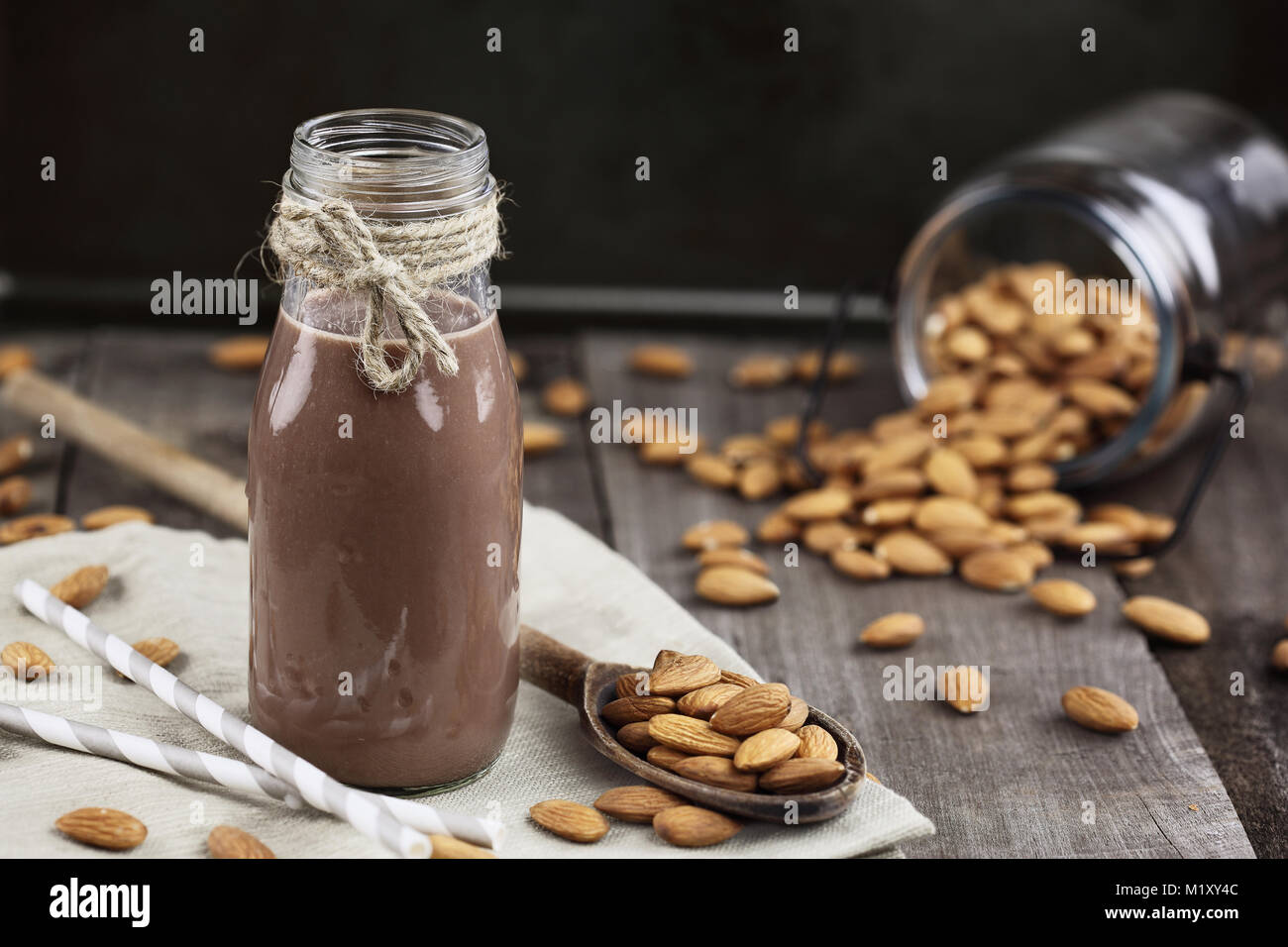 Schokolade Mandel Milch in ein Glas Flasche mit ganzen Mandeln über einen rustikalen Holztisch verschüttet. Stockfoto