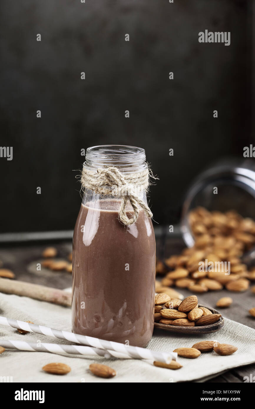 Organische Schokolade Mandel Milch in ein Glas Flasche mit ganzen Mandeln über einen rustikalen Holztisch verschüttet. Stockfoto