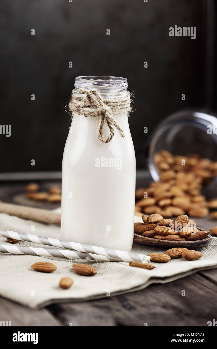 Organische weiße Mandelmilch in einer Glasflasche mit ganzen Mandeln über einen rustikalen Holztisch verschüttet. Stockfoto