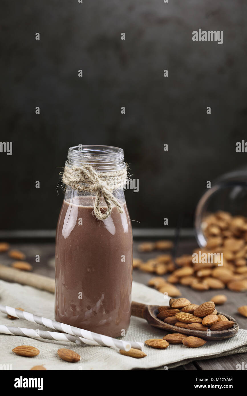 Organische Schokolade Mandel Milch in ein Glas Flasche mit ganzen Mandeln über einen rustikalen Holztisch verschüttet. Stockfoto