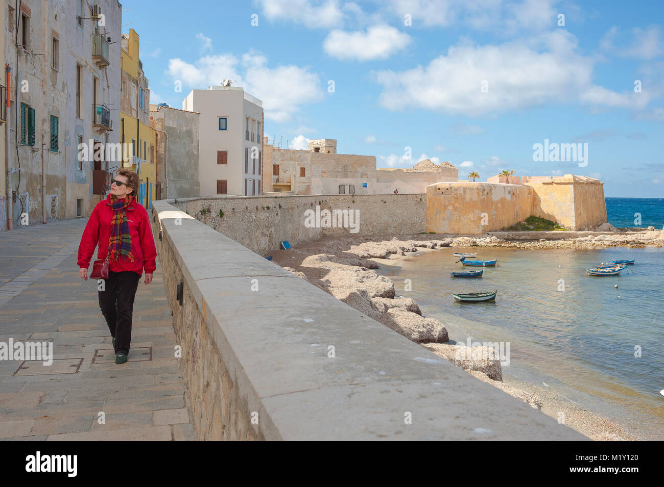 Frau solo Tourist allein Konzept, Blick auf eine reife Frau Reisende zu Fuß entlang der Meeresmauer am Nordufer von Trapani, Sizilien. [MODELL FREIGEGEBEN] Stockfoto