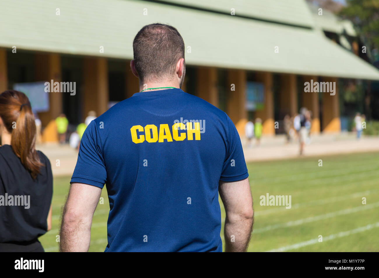 Rückseite der männlichen Athleten, Trainer in Deep Blue T-Shirt mit gelbem Trainer Wort auf dem Rücken, im Freien in einem Sport Feld geschrieben Stockfoto