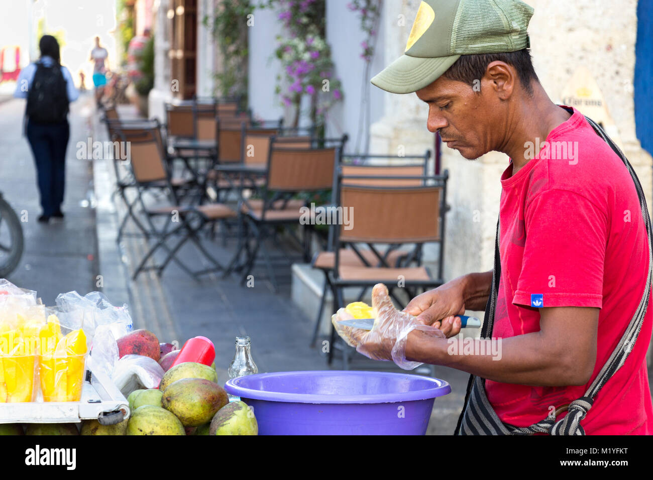Cartagena, Kolumbien - Januar 23th, 2018: eine Frucht street Hersteller schneiden Mango stehen auf der Straße mit seinem Holz- Warenkorb mit Früchten in Cartagena. Stockfoto