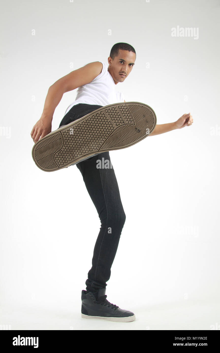 Ein junger Mann in einem gemischten Rennen weiß Kurzarm Shirt und schwarze Jeans kicking seinen Schuh in die Kamera auf einem isolierten Hintergrund Stockfoto