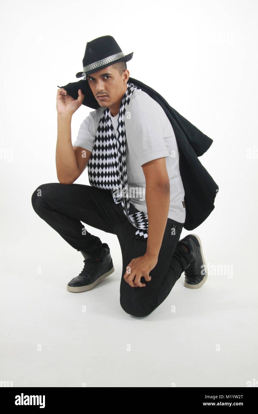 Jungen gemischten Rennen Männer tragen ein weißes Kurzarm shirtt, schwarze Jeans, karierten Schal und Hut hocken auf einem isolierten Hintergrund Bei t starrte Stockfoto