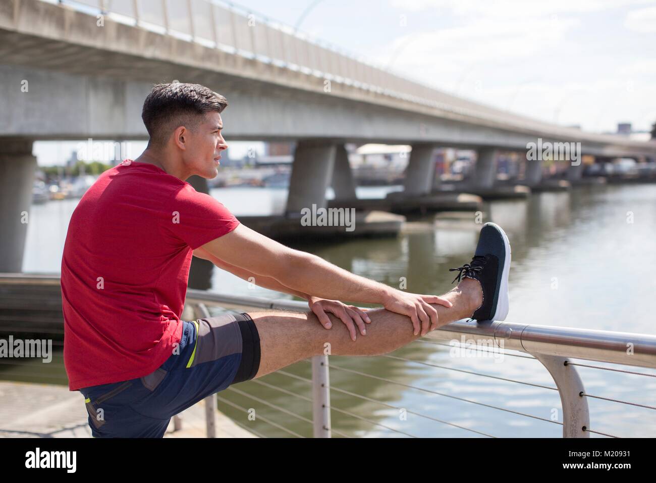 Junger Mann stretching Bein auf dem Geländer vor einem Lauf. Stockfoto