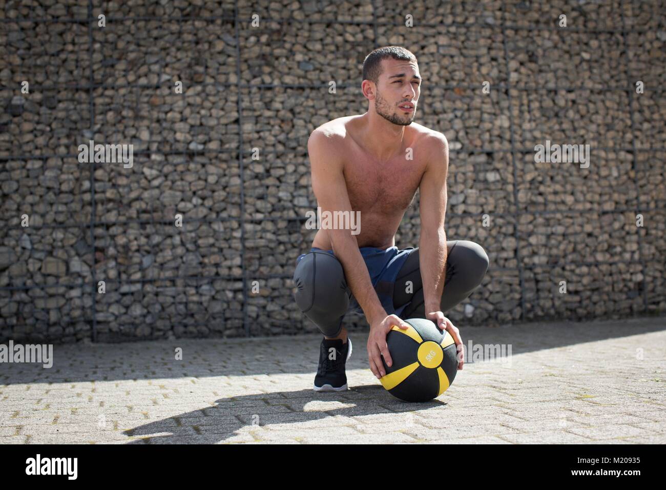 Junger Mann zusammengekauert mit medizinball. Stockfoto