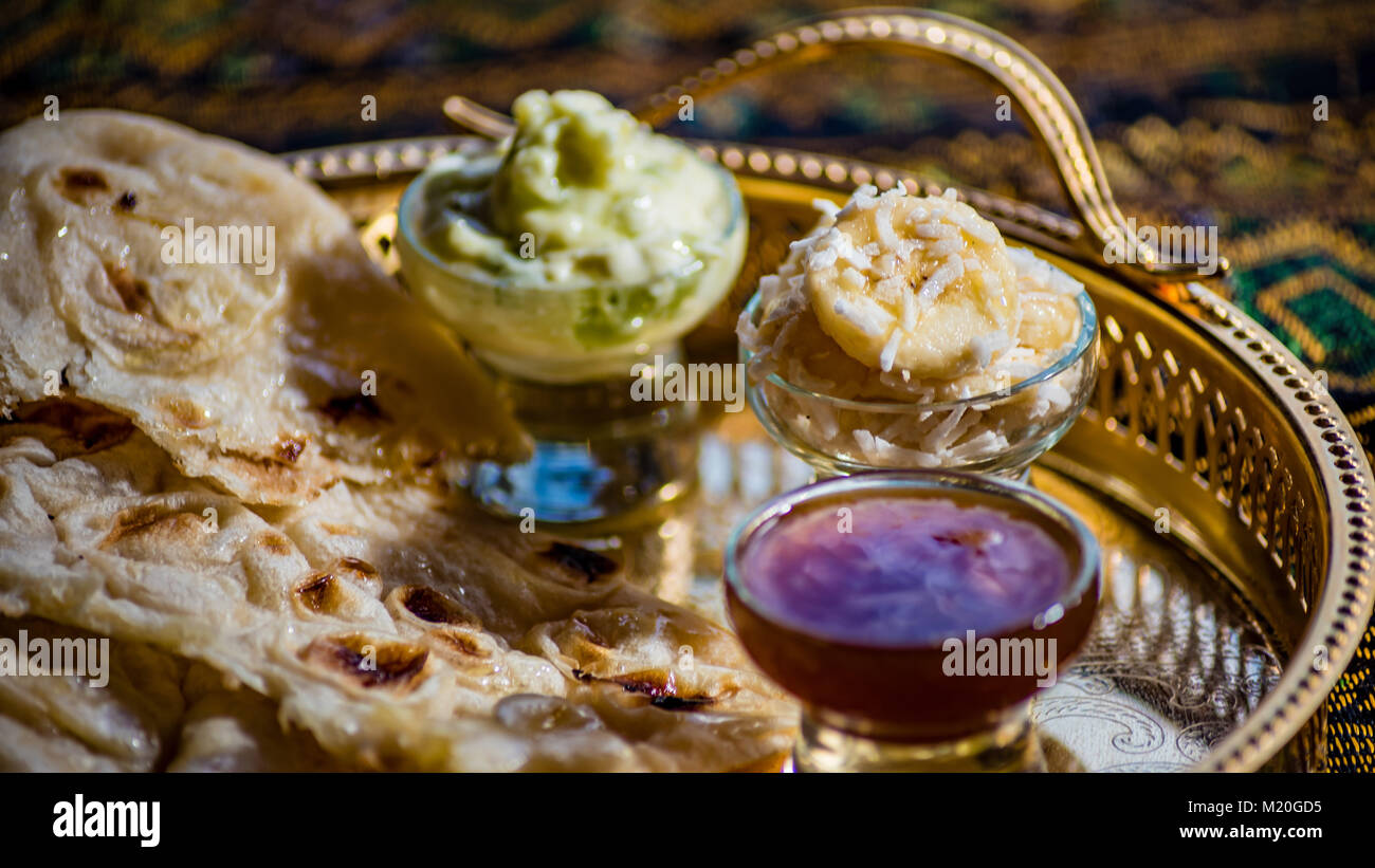 Bunte indische Essen, Naan Brot, Chutney, Banane. Seitenansicht des lebhaften Mittag- oder Abendessen, Fladenbrot, Glasschalen, rote und grüne Soßen, goldene Platte. Stockfoto