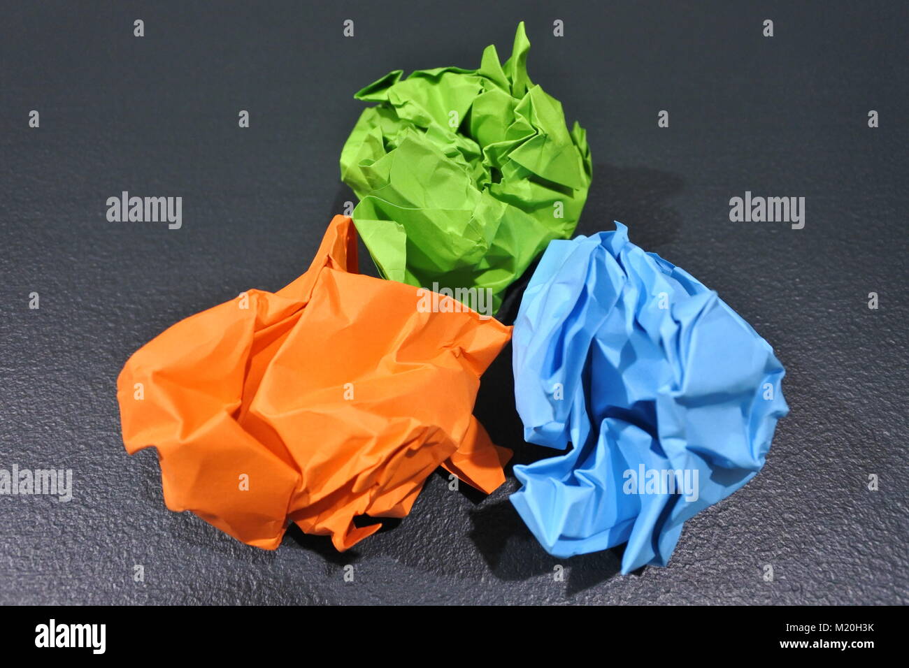 Eine lebendige Darstellung der Kreativität: Drei zerknitterte Papierkugeln in Orange, Hellgrün und Hellblau, kunstvoll in einer Dreiecksform auf einem T angeordnet Stockfoto