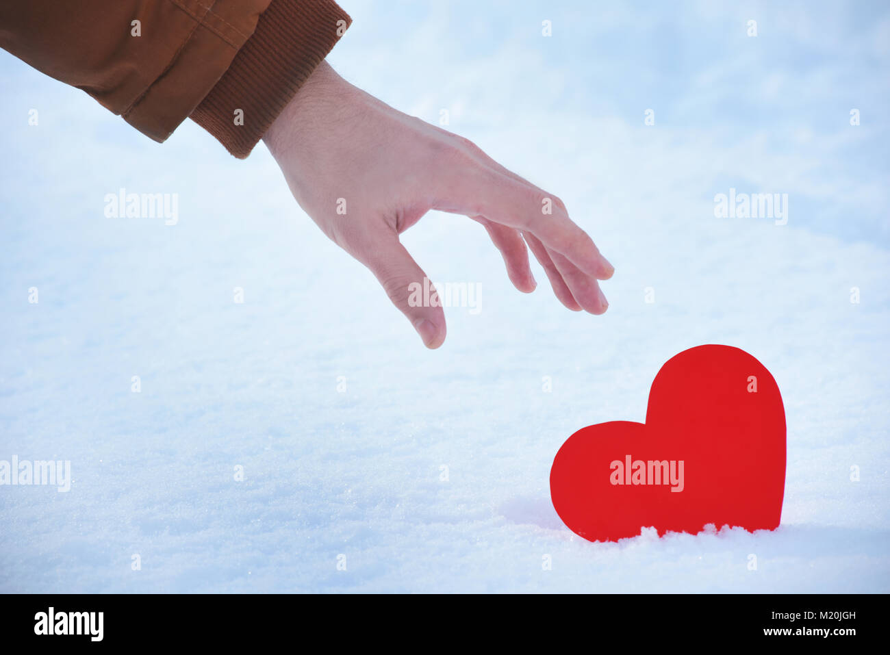 Verloren rotes Herz ist allein auf ein Valentinstag, Herz an einem kalten Winter Schnee, mit einem strahlenden Licht um. Hand herauf ein rotes Herz aus dem Schnee wit Stockfoto