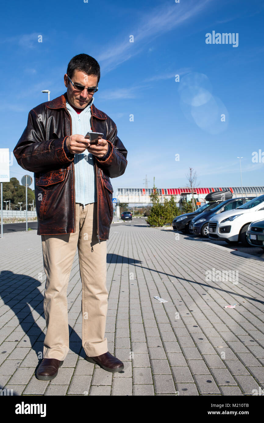 Im mittleren Alter Kaukasischer mann Kontrolle Smartphone während des Wartens auf einen Termin in einer Autos parken. Stockfoto
