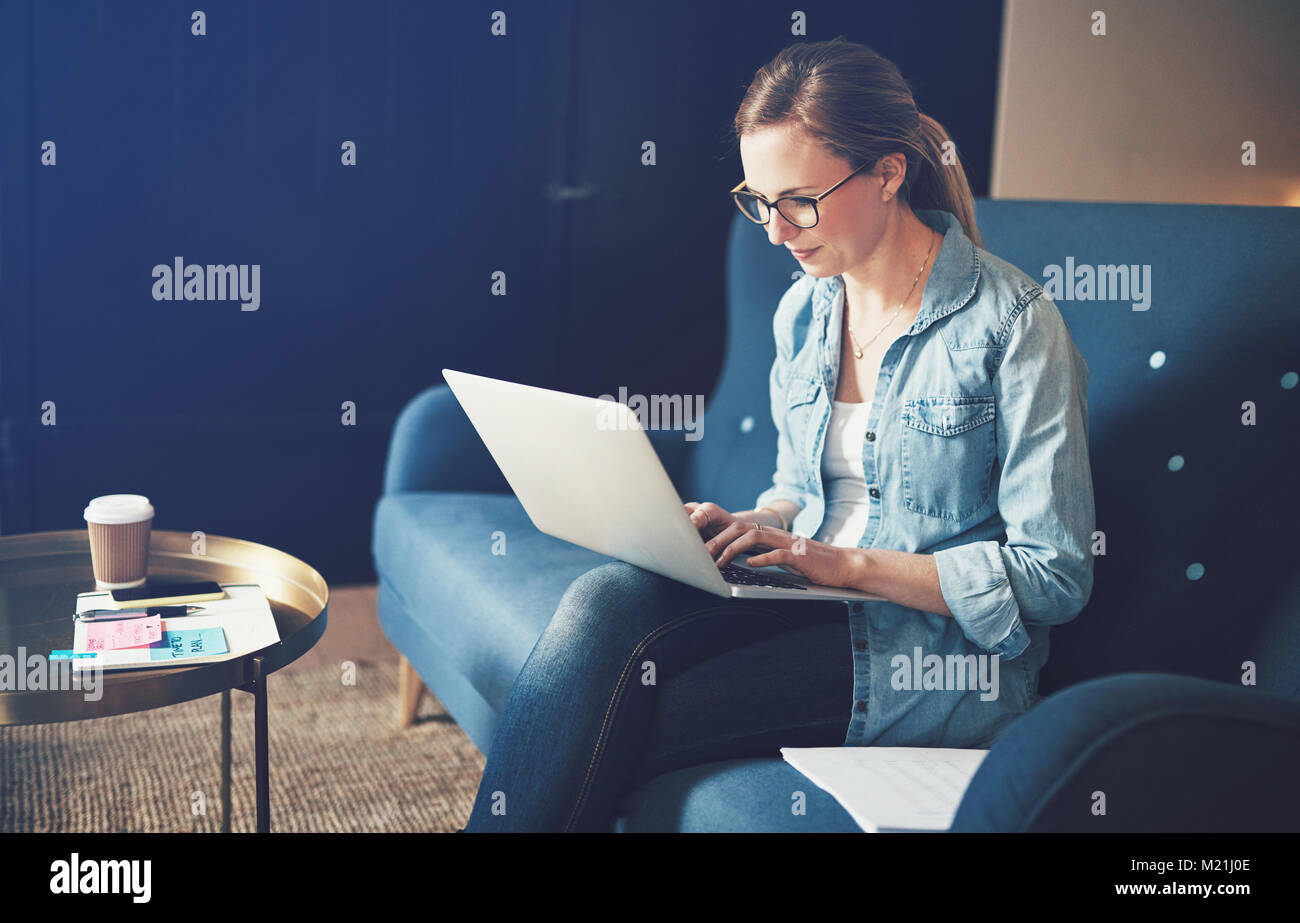 Lächelnde junge weibliche Unternehmer Surfen online mit einem Laptop beim Sitzen auf Ihrem Sofa von zu Hause aus arbeiten Stockfoto