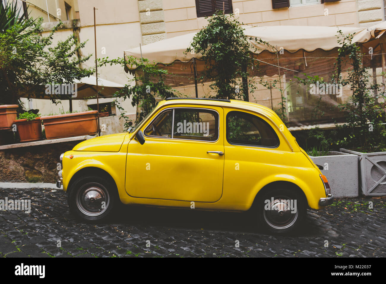 Eine gelbe kleine Auto in einer römischen Straße mit Steinen und Pflanzen im Hintergrund Stockfoto