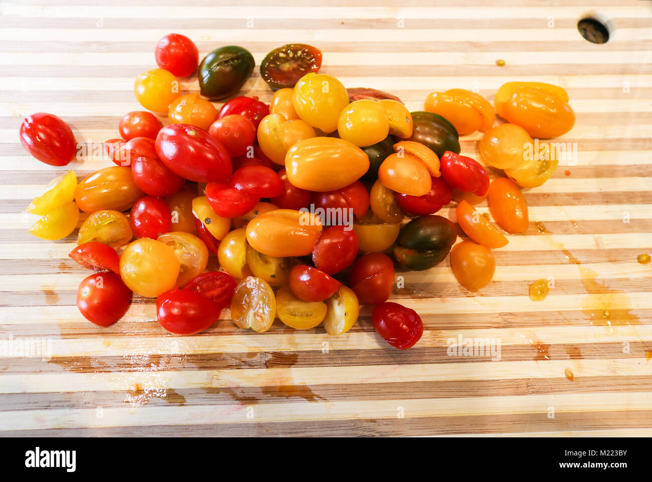 Ein Haufen von saftig bunte Trauben Tomaten in der Hälfte auf einem stiped Holz Schneidebrett bereit zu Gericht, gehackt Stockfoto
