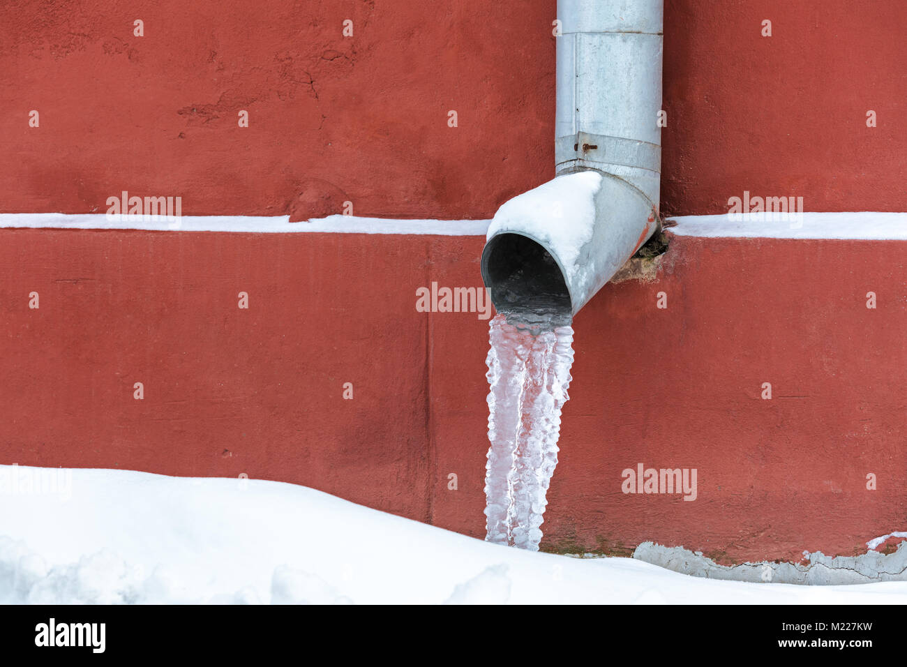 Gefrorenes Wasser in einem abflußrohr im Winter gegen rote grunge Wand Hintergrund Stockfoto