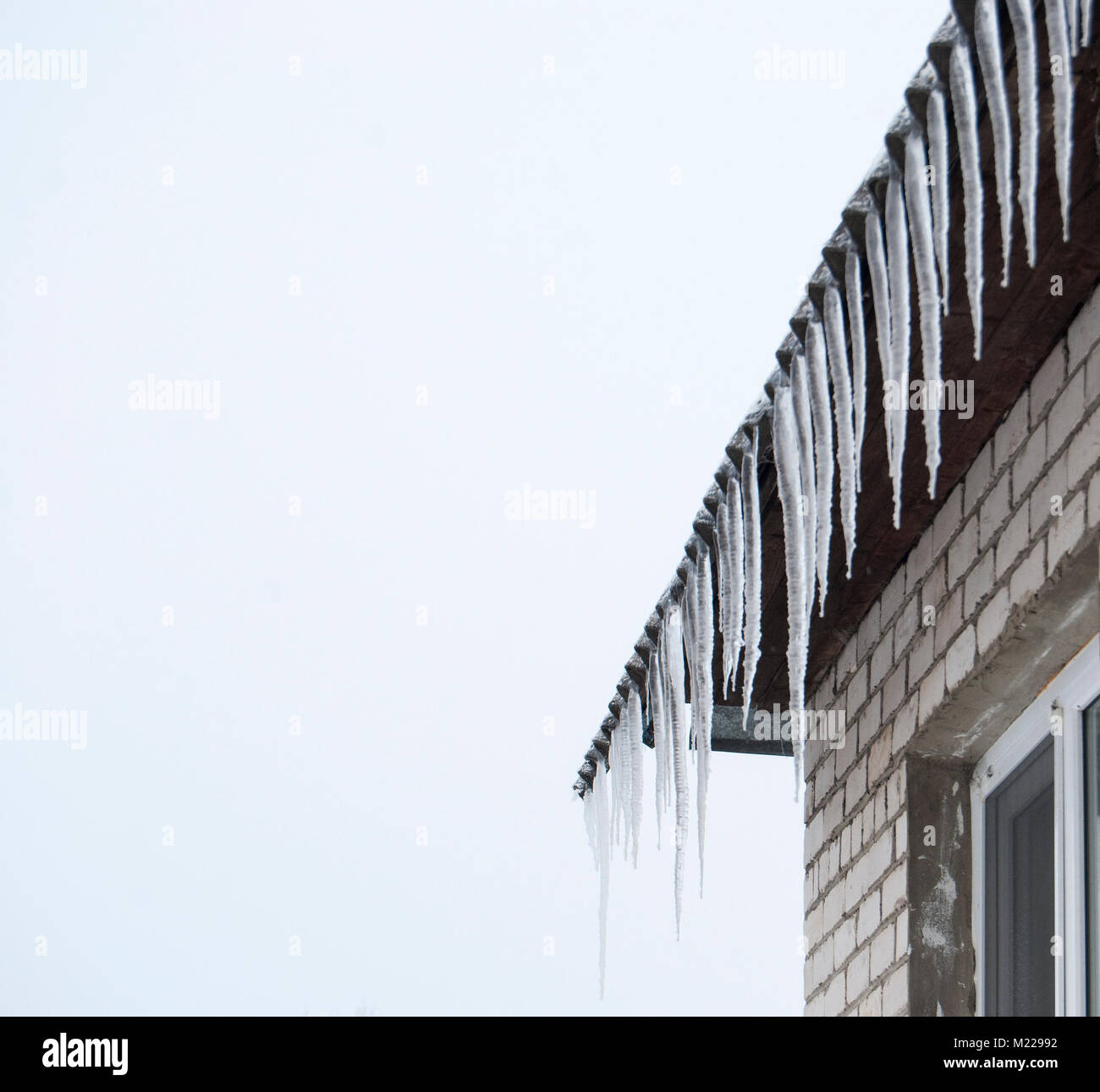 Eiszapfen hängen von dem Dach von einem Haus im Dorf im Winter. Stockfoto