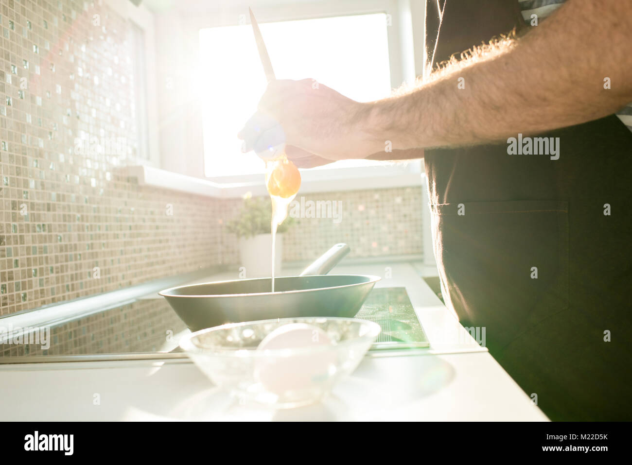 Seitenansicht der männlichen Händen Eier in die Pfanne beim Kochen Frühstück in der modernen Küche, die durch Sonnenlicht beleuchtet brechen Stockfoto