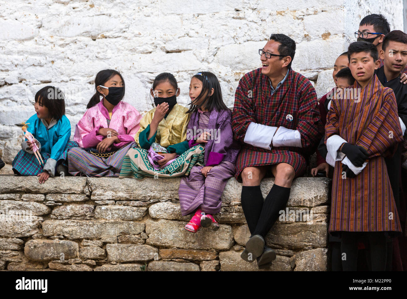 Prakhar Lhakhang, Bumthang, Bhutan. Junge bhutanische Mädchen in traditioneller Kleidung, mit Atemschutzmasken. Männer in der Gho, der traditionellen Männer Kleidungsstück. Stockfoto