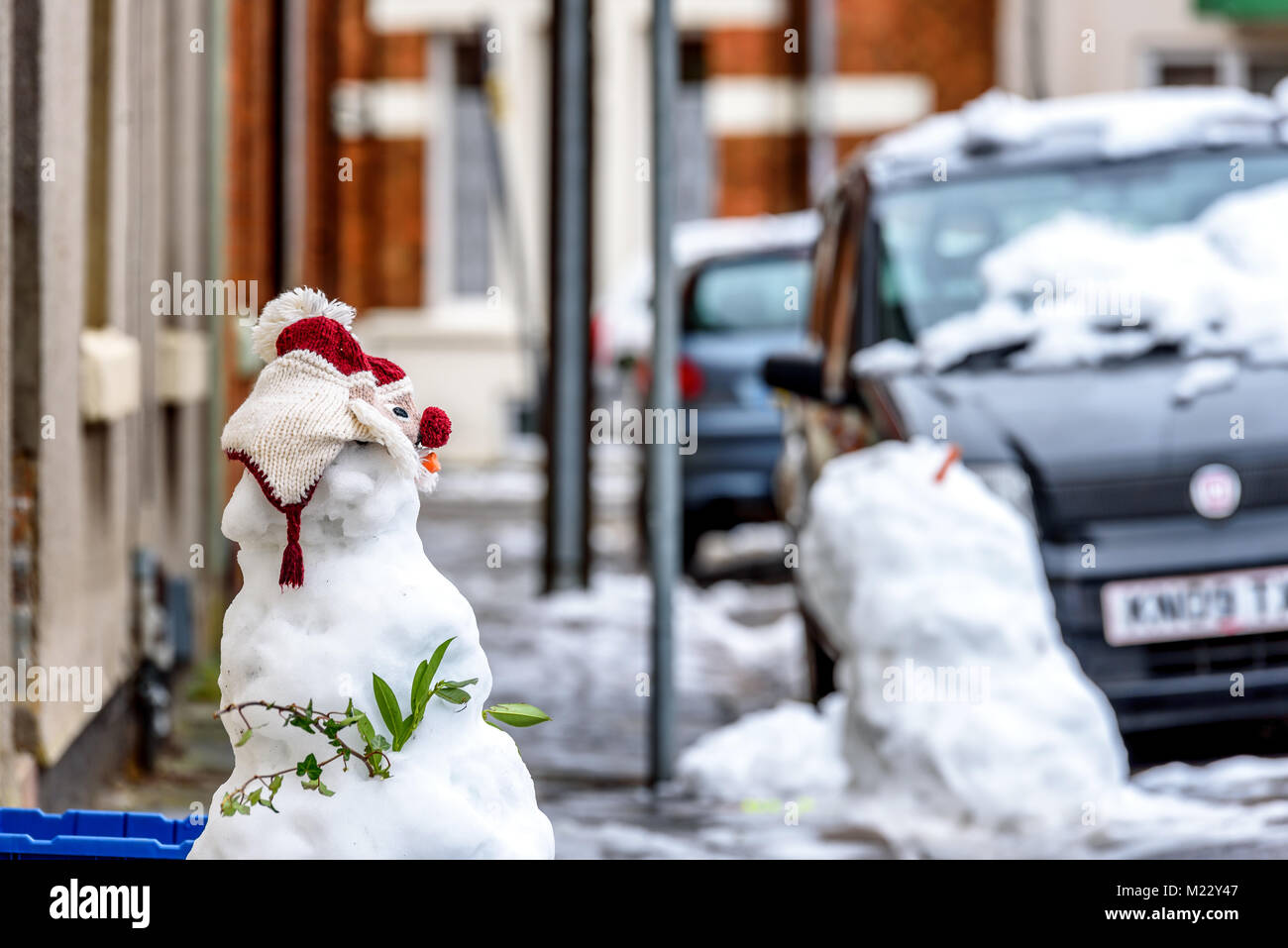 Bewölkt winter Tag der selbstgemachten Schneemann auf typisch britische Straße Fußweg neben dem Papierkorb leeren Kästen Stockfoto