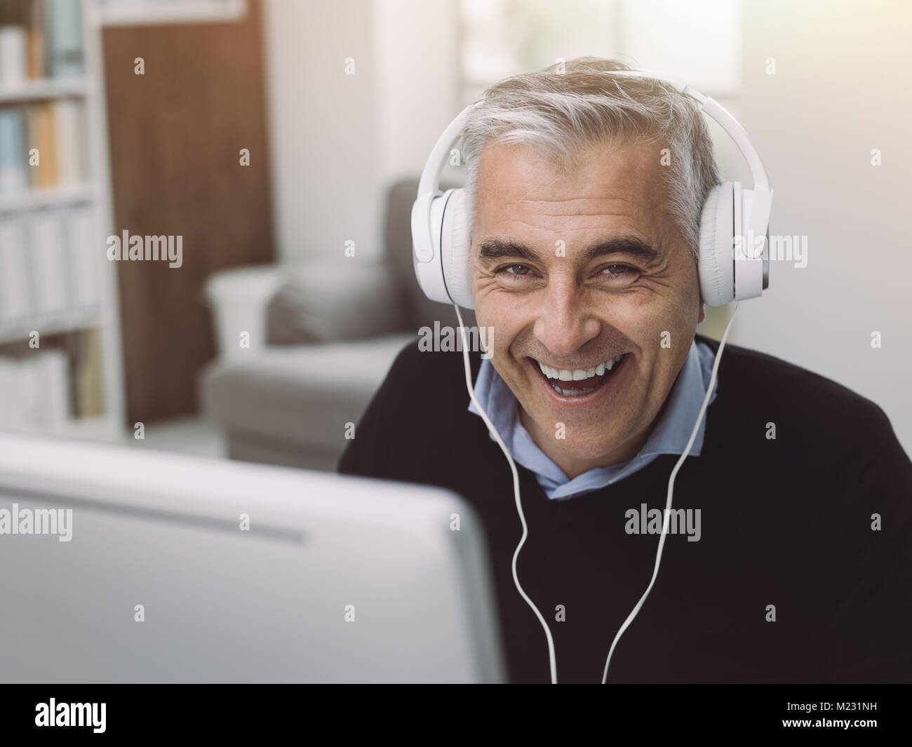 Glücklicher Mann Kopfhörer tragen und Filme in seinem Home Office Online, genießt er und lächelnd Stockfoto