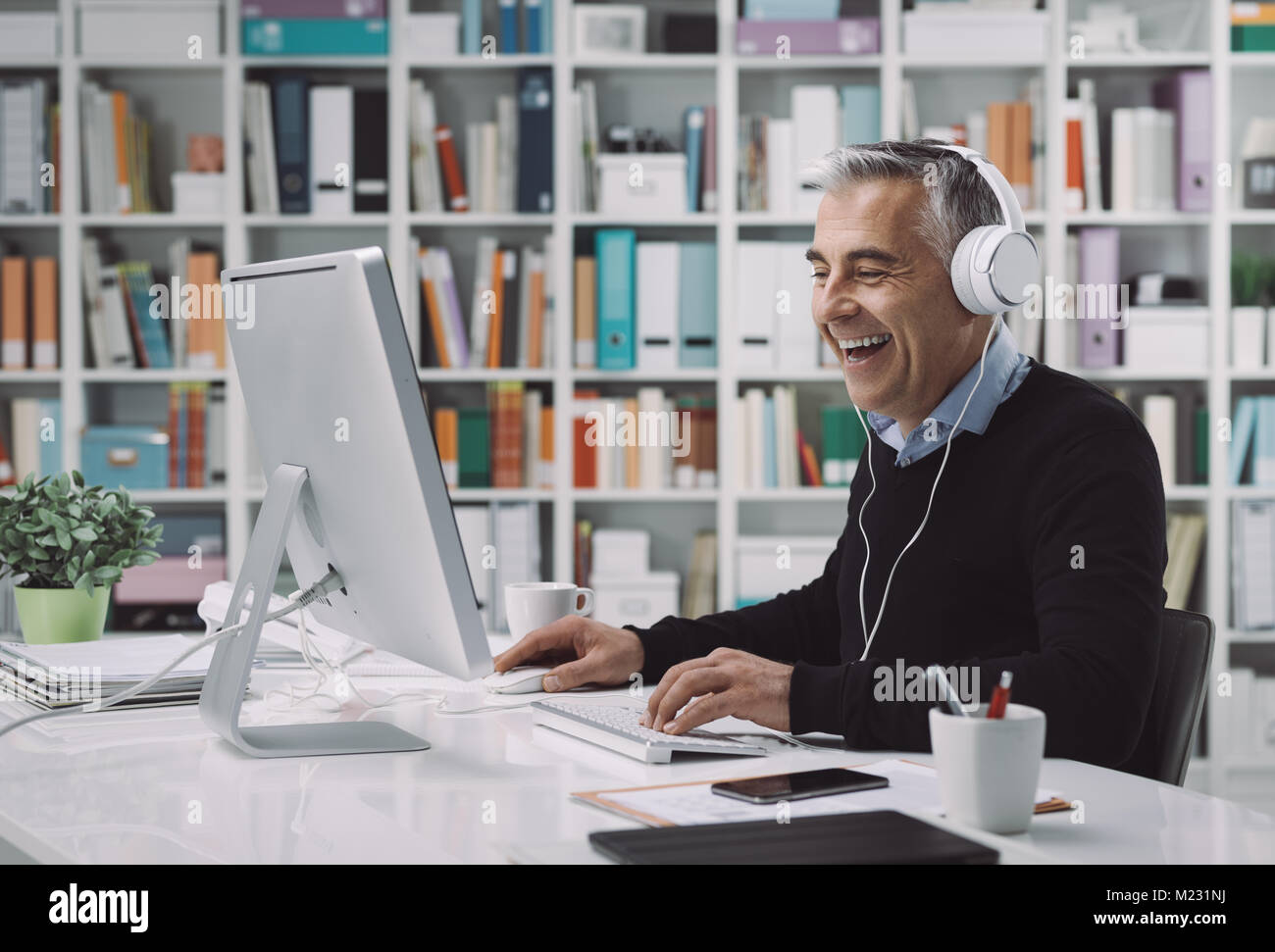 Glücklicher Mann Kopfhörer tragen und Filme in seinem Home Office Online, genießt er und lächelnd Stockfoto