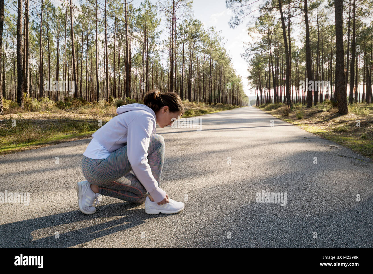 Frau Läufer tun Ihre Schnürsenkel vor Jogging entlang einer Forststraße. Stockfoto