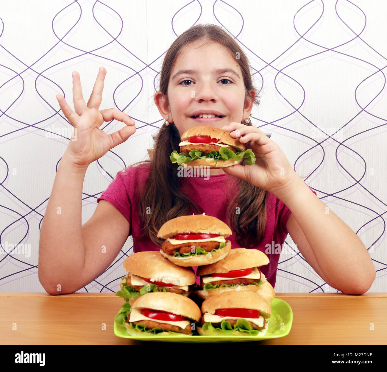 Glückliche kleine Mädchen mit Hamburger und ok Handzeichen Stockfoto
