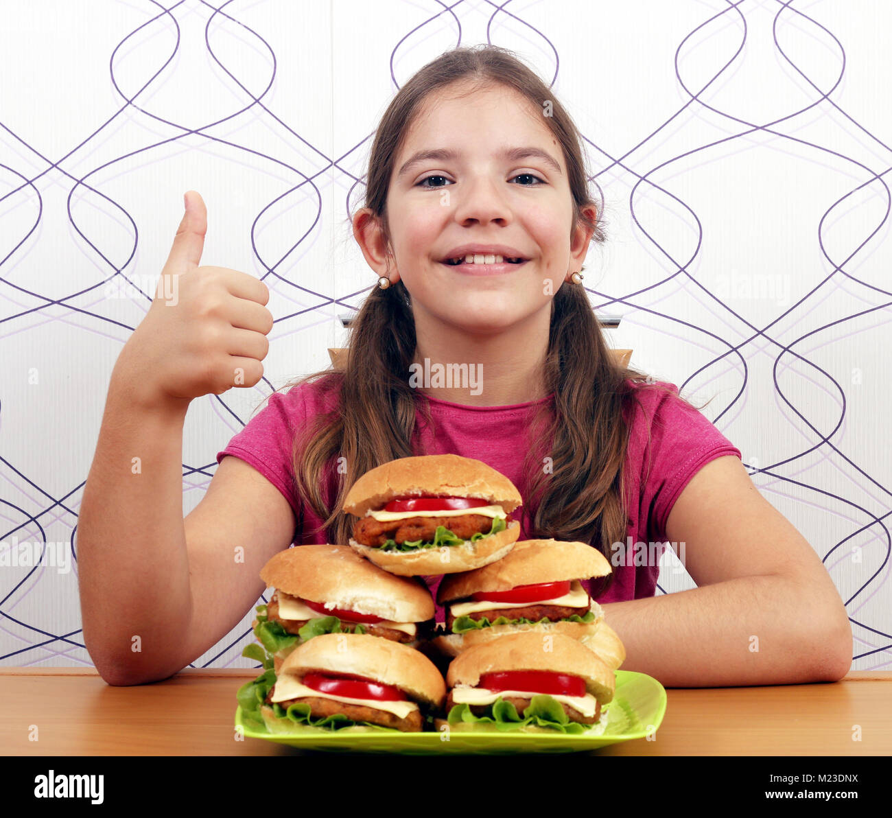 Glückliche kleine Mädchen mit Hamburger und Daumen hoch Stockfoto