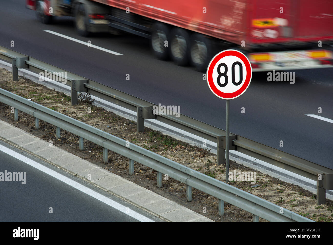 Verkehrsschild zeigt 80 km/h Höchstgeschwindigkeit auf einer Autobahn mit roten Lkw im Hintergrund fahren Stockfoto