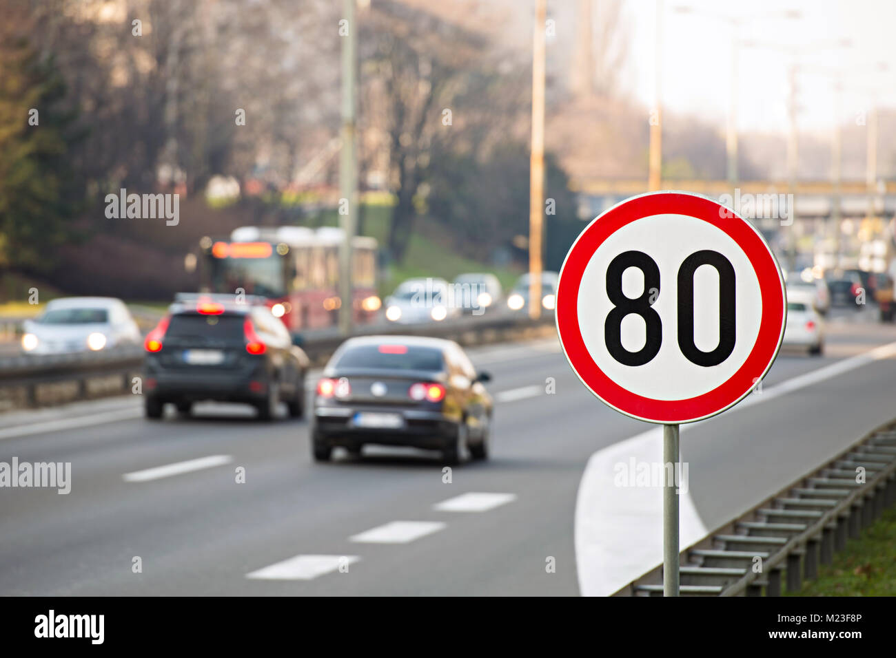 Verkehrsschild zeigt 80 km/h Höchstgeschwindigkeit auf der Autobahn voller Autos Stockfoto