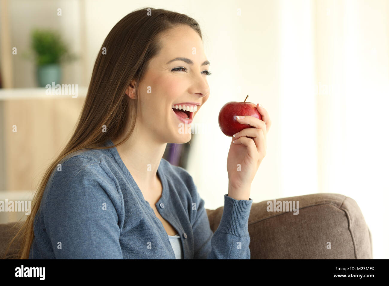 Glückliche Frau essen eine Apple entfernt, sitzen auf einer Couch im Wohnzimmer zu Hause Stockfoto