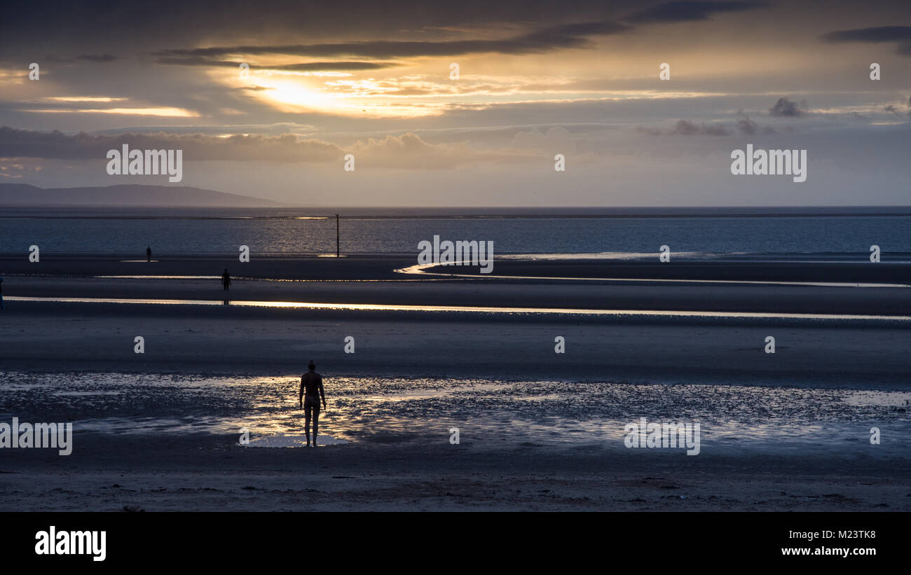 Liverpool, England, UK - 12. November 2016: Die Sonne hinter Antony Gormley' Skulpturen einen anderen Ort' auf Crosby Strand, mit den Bergen von Sno Stockfoto